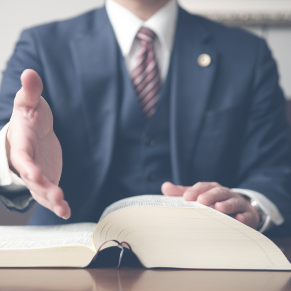 Photo of a man in a suit holding out his outstretched hand and an open book on the table